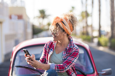 Side view of young woman using mobile phone while sitting in city