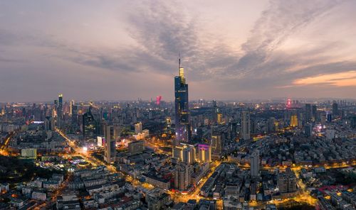 Illuminated buildings in city against cloudy sky