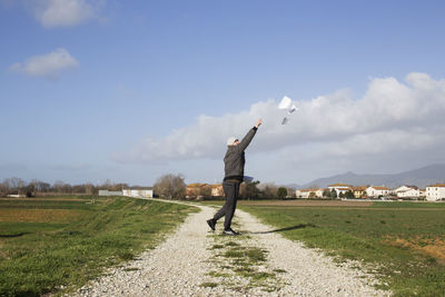 Side view of man throwing paper while standing on field against sky