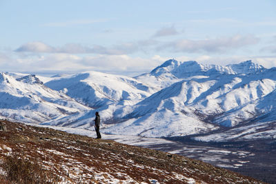 Scenic view of snowcapped mountains against sky with solo traveler