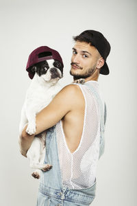 Portrait of young man carrying dog against white background