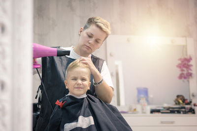 Female barber styling hair of boy at salon