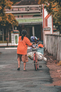 Rear view of man riding bicycle on road against building