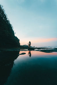 Reflection of man in sea against sky during sunset