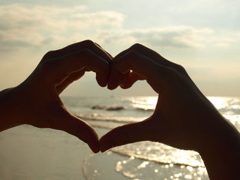 Close-up of hand holding heart shape against sea