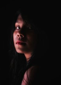 Close-up portrait of young woman against black background