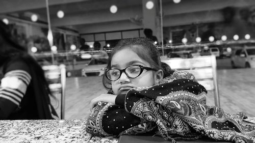 Sad girl wearing eyeglasses sitting on table