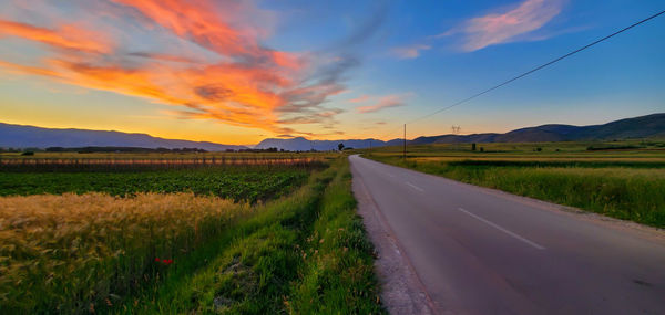 Road amidst field against sky during sunset