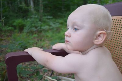 Close-up of shirtless baby boy sitting on chair at yard