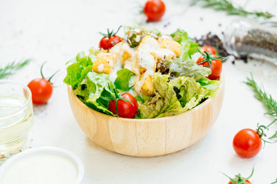 Close-up of salad in bowl amidst cherry tomatoes and rosemary on table