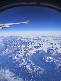 Aerial view of airplane flying over snowcapped landscape against blue sky