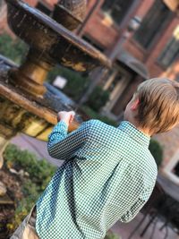 Rear view of boy holding coin while standing by fountain