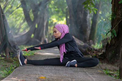 Side view of woman sitting on street amidst trees in forest