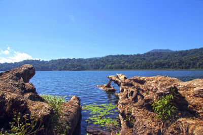 Rocks by lake against clear blue sky