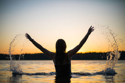 Beautiful girl in a long black swimsuit swims on the lake in the rays of sunset or dawn