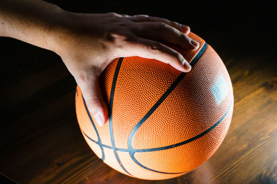 Cropped image of man holding basketball on floor in dark