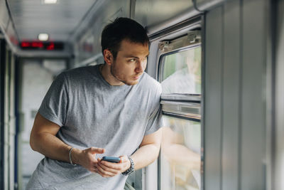 Man holding smart phone leaning on window of railroad car