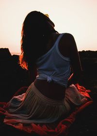 Rear view of woman sitting against sky during sunset