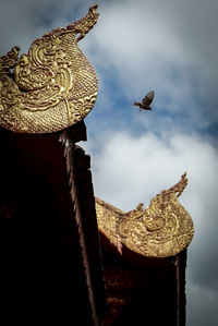 Close-up of bird perching on statue against sky