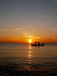 Silhouette people in sea against sky during sunset