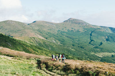 Rear view of people walking by mountain against sky