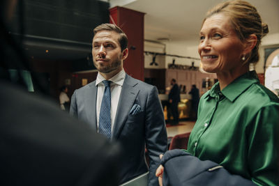 Young businessman standing by smiling businesswoman in hotel lounge