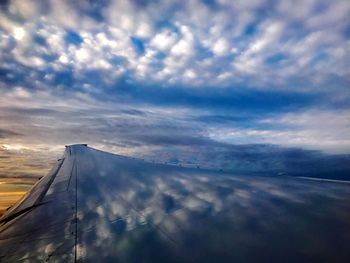 Close-up of airplane wing flying over clouds during sunset
