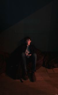 Full length portrait of young man sitting against black background