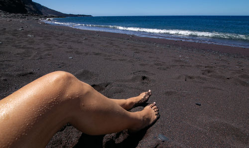 Low section of woman lying on beach against sky