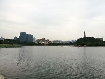 Calm river with buildings in background against sky