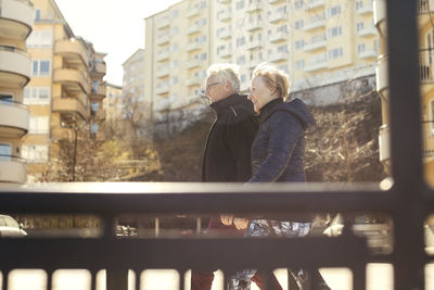 Smiling senior couple walking on roadside against buildings in city