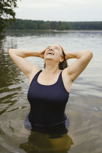 Happy senior woman with head in hands against river