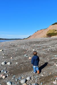 Rear view of boy on land against clear blue sky