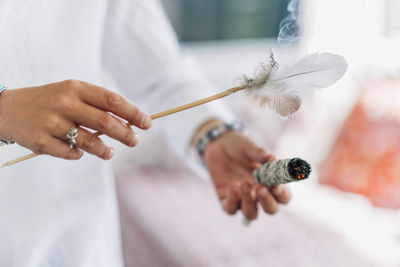 Midsection of sage holding feather with smudge stick while standing indoors