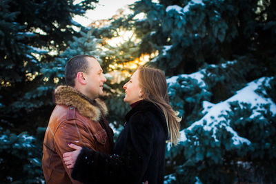 Side view of couple standing against snow covered trees during winter