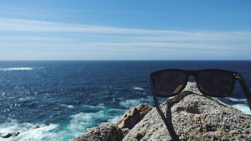 Close-up of sunglasses on rock by sea against sky