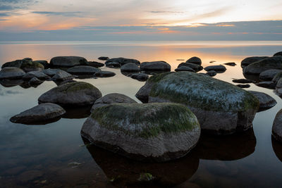 Rocks on beach against sky during sunset