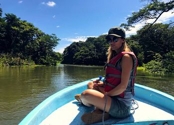 Woman sitting on boat in river against sky