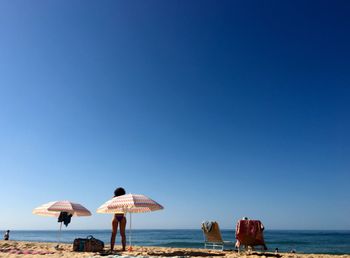 Rear view of woman standing at beach against clear blue sky