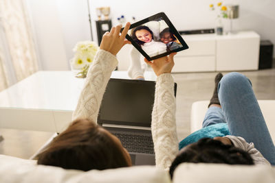 Friends doing video call while lying down on sofa at home