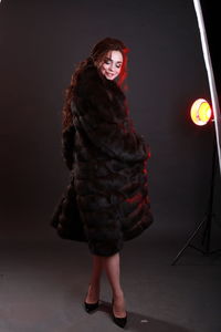 Fashionable young woman wearing fur jacket while standing against gray background