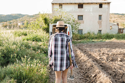 Rear view of woman walking with equipment in farm