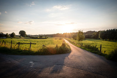 Dirt road amidst field against sky during sunset