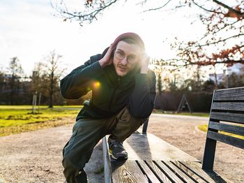 Portrait of young man crouching on bench in park