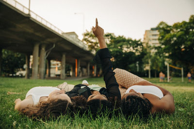 Teenage girl with hand raised pointing while lying amidst friends on grass at park