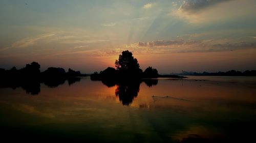 Silhouette trees reflection in lake against sky during sunrise