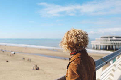 Rear view of woman standing by railing on scheveningen pier at beach against sky
