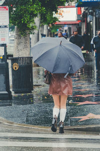 Attractive young woman walks down a rainy street with a plain black umbrella and white skirt.