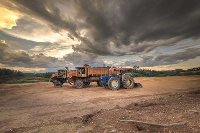 Tractor and trucks on field against sky during sunset