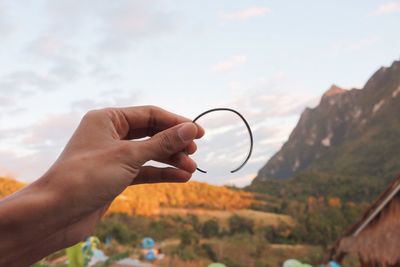 Close-up of woman holding bracelet against sky